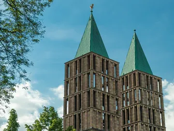 Zwei Türme mit grünem Dach, vor blauem Himmel.