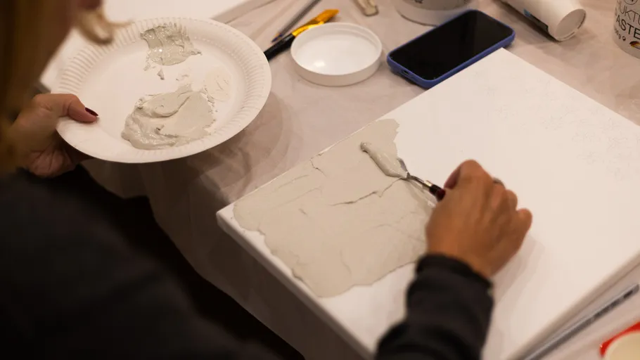 Person trägt Gips mit einem Messer auf Leinwand auf.