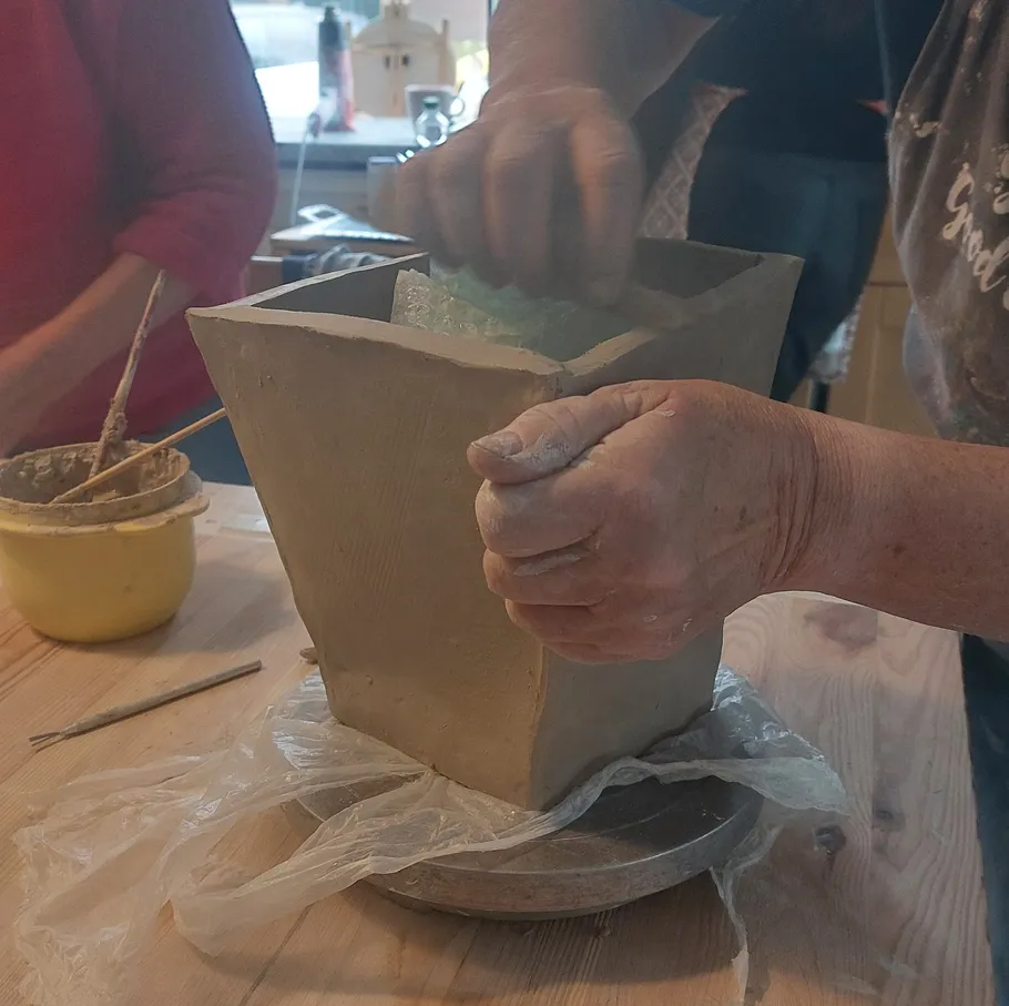 Hände formen Tonvase auf Holztisch.