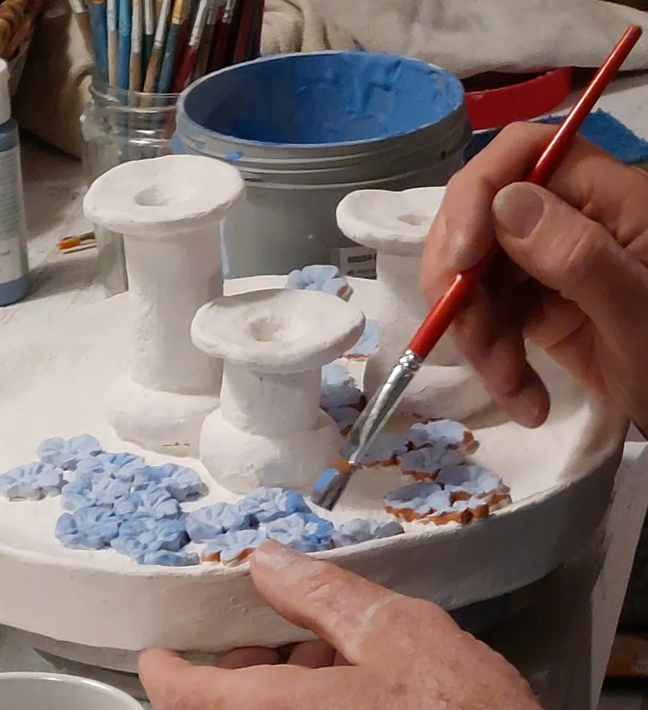 Person painting ceramic art with blue flowers.