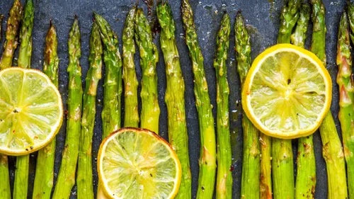 Gegrillter Spargel mit Zitronenscheiben auf Schiefer.