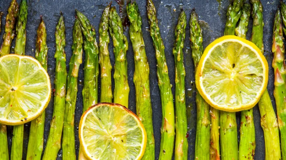 Gegrillter Spargel mit Zitronenscheiben auf Schiefer.