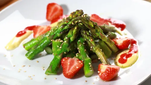 Asparagus with strawberries and sauces on plate.