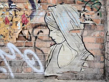 Wall painting depicts a woman with a hood, in an urban environment.