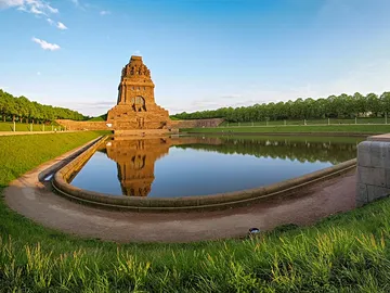 Ein Denkmal spiegelt sich im ruhigen Wasser eines Beckens.