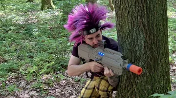 Person zielt mit Spielzeuggewehr hinter Baum draußen.