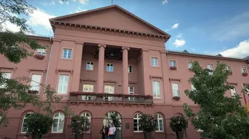 Rosa Gebäude mit Säulen und Bäumen davor.