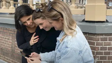 Drei Frauen betrachten Smartphone im Freien.