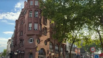 Historisches rosa Gebäude mit Bäumen und Straße.