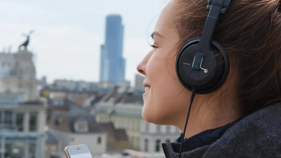 Woman enjoying music on headphones, city background.