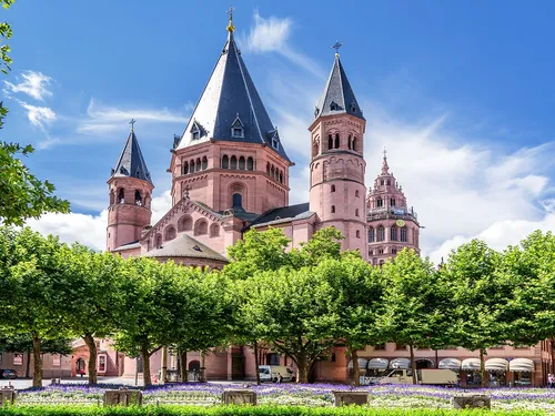 Rose red church with towers surrounded by green trees.