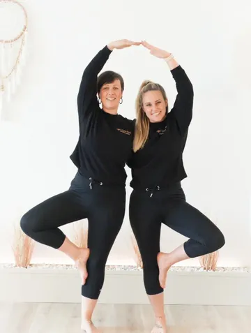Zwei Frauen praktizieren gemeinsam Yoga drinnen.