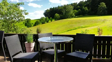 Terrasse mit Stühlen, Tisch, Blick auf grünen Hang.