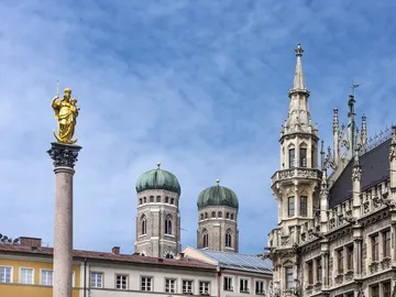 Golden statue on column, historic buildings in the background.