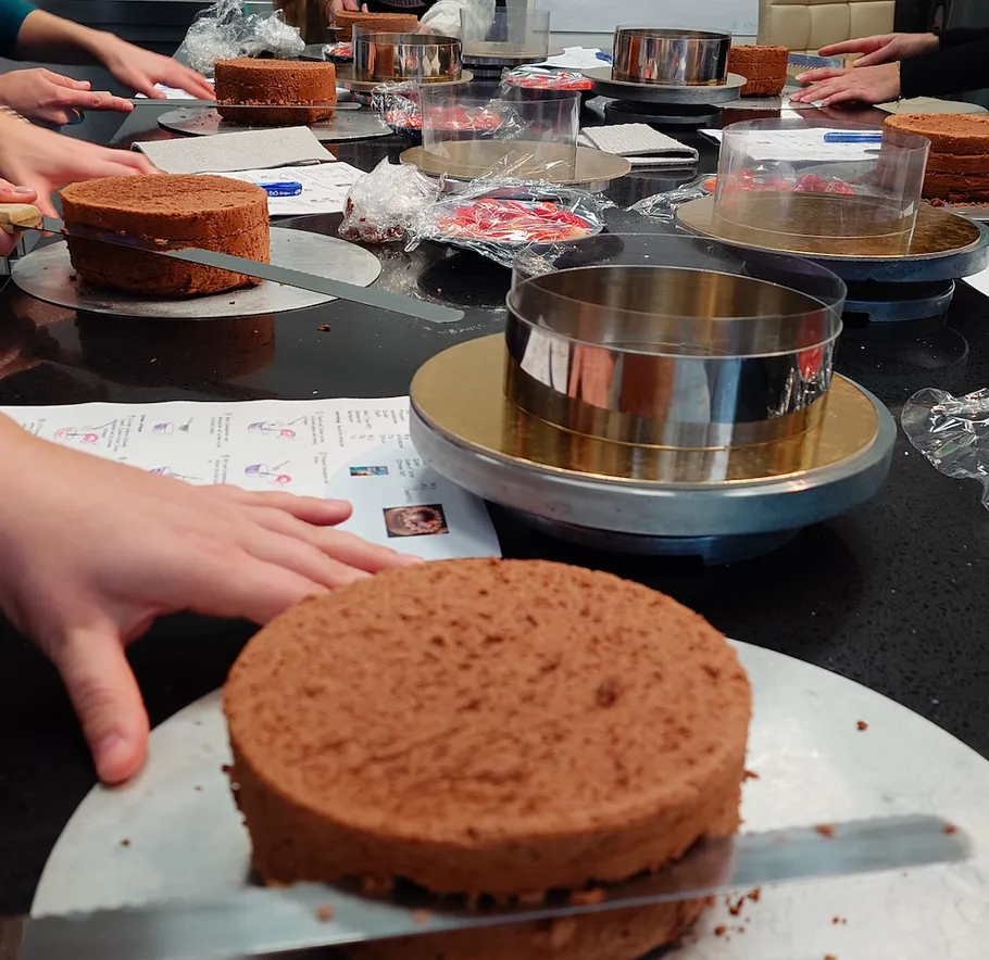 Hands slicing cakes on a black table.