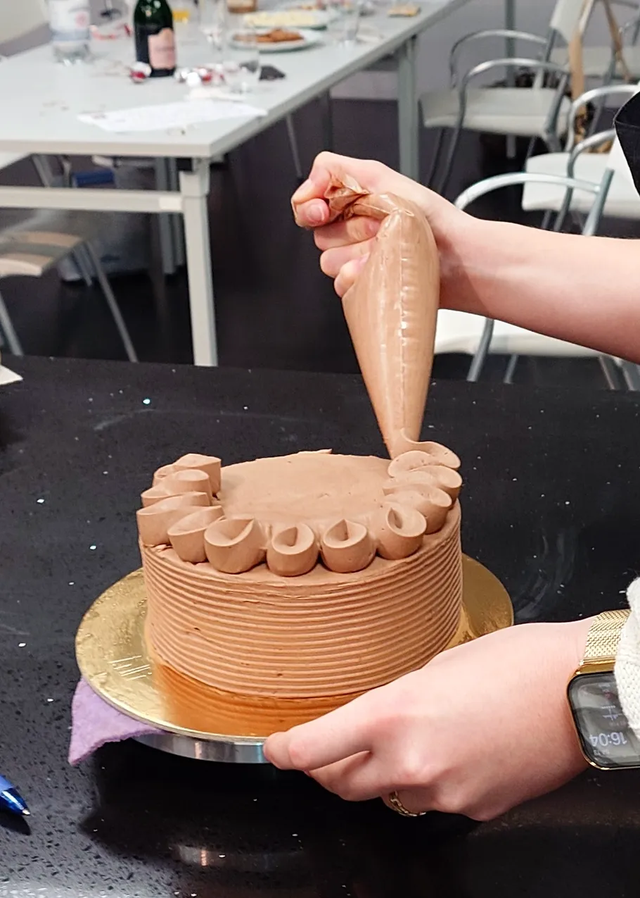 Person decorating chocolate cake in kitchen.