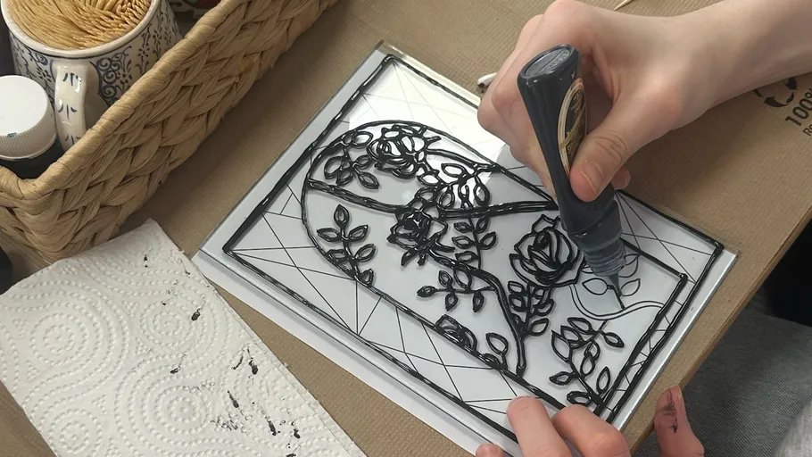Person tracing floral design with black paint.