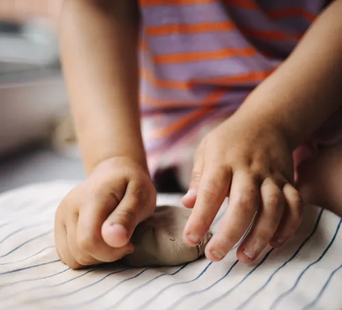Child shaping clay with hands indoors.