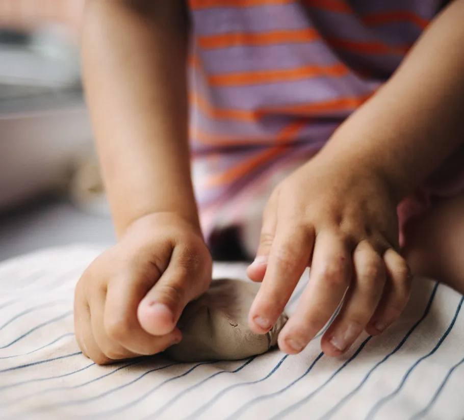 Child shaping clay with hands indoors.