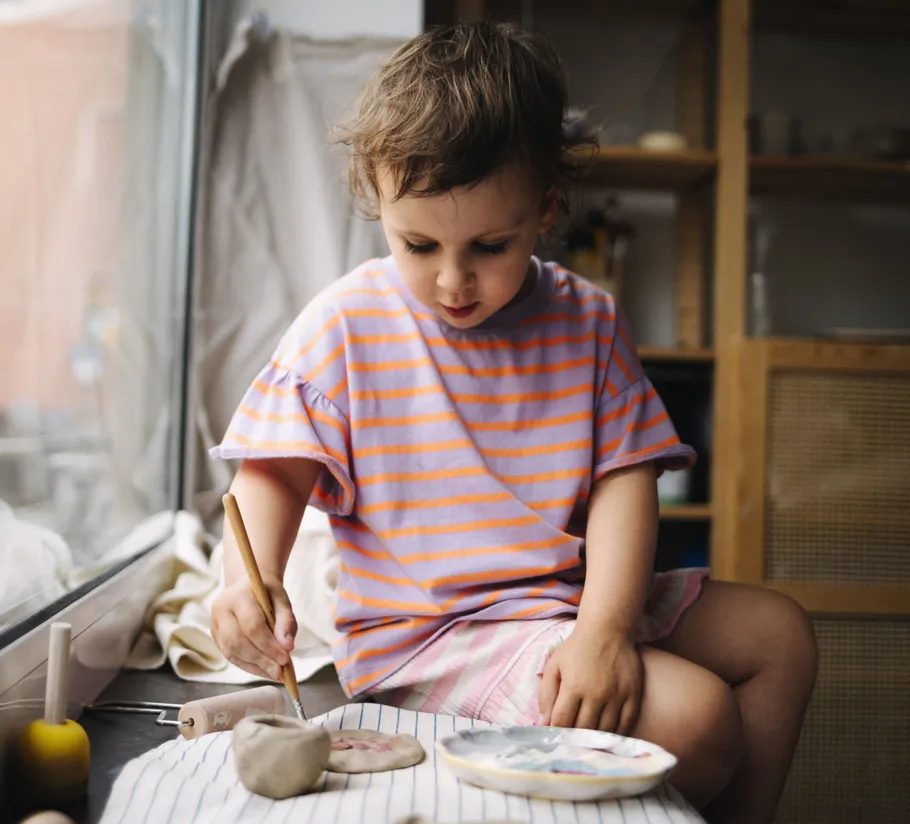 Child painting on clay near a window.