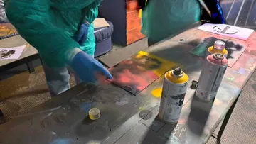 Hands spray-painting on a table indoors.