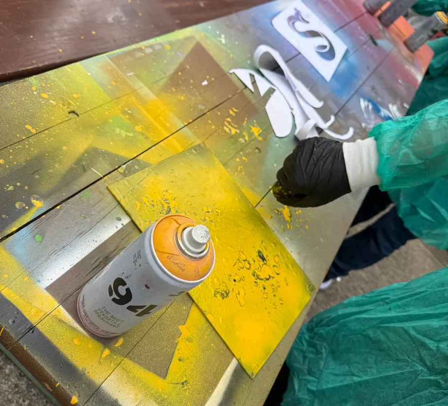 Person sprayt Schablonen auf bunte Oberfläche.