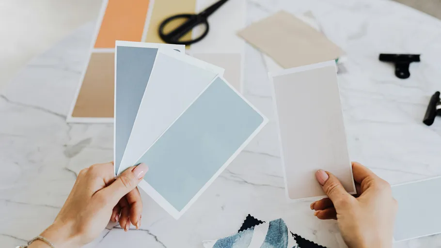 Hands holding paint swatches on marble table.
