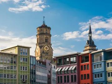 A tower with a dial stands between modern buildings.