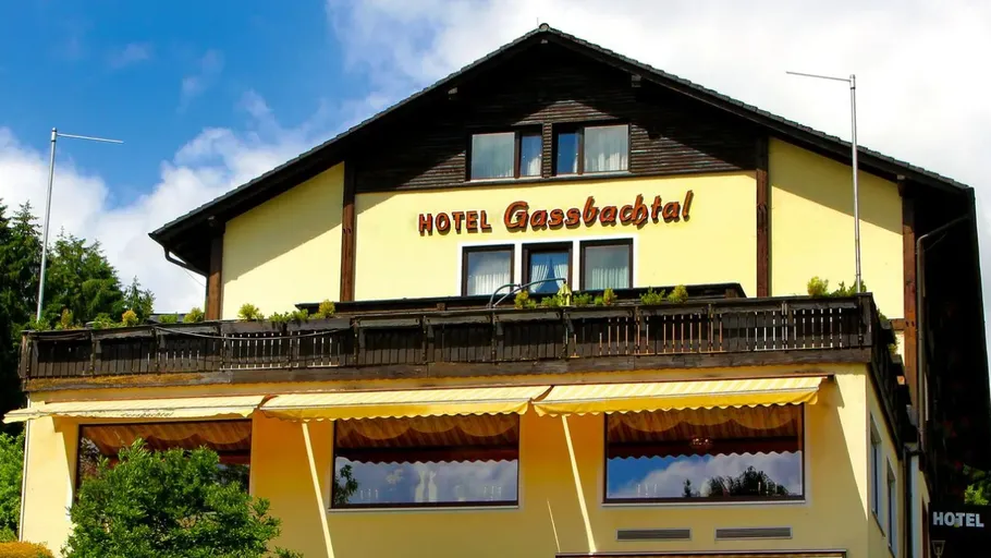 Hotelgebäude mit Balkon, umgeben von Bäumen.