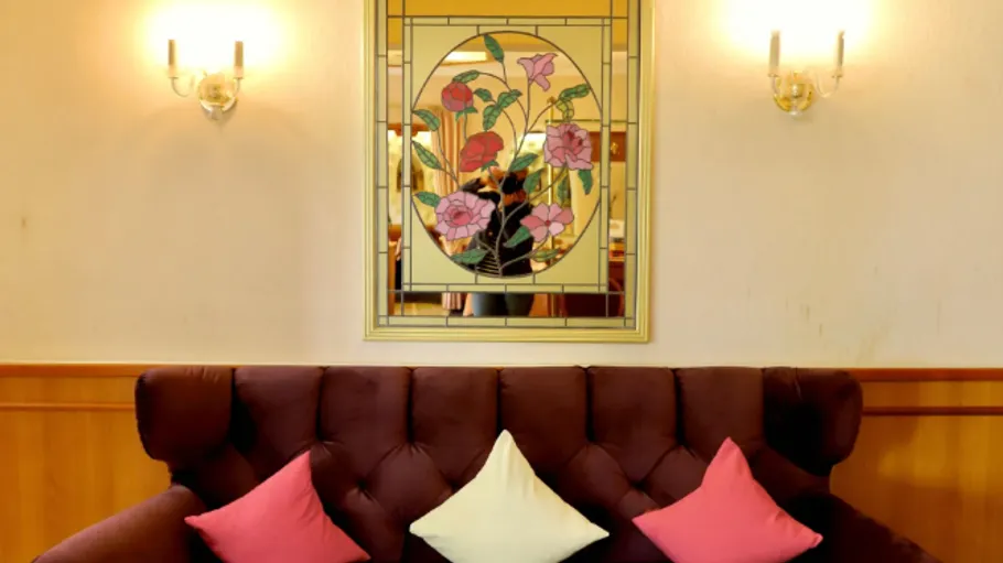 Couch with colorful pillows beneath stained glass window.