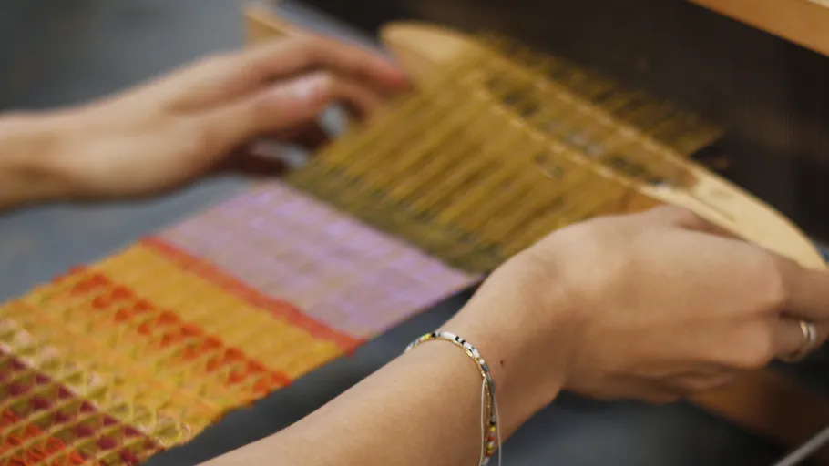 Hands weaving colorful fabric on a loom.