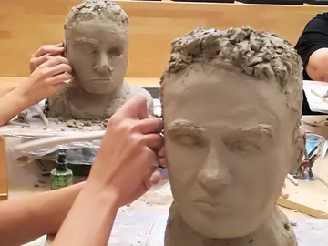 Clay heads are worked on by people in a workshop.
