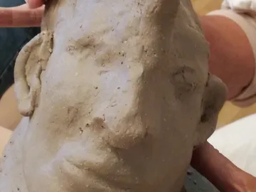 Sculpture of a head made of clay, held by hands.