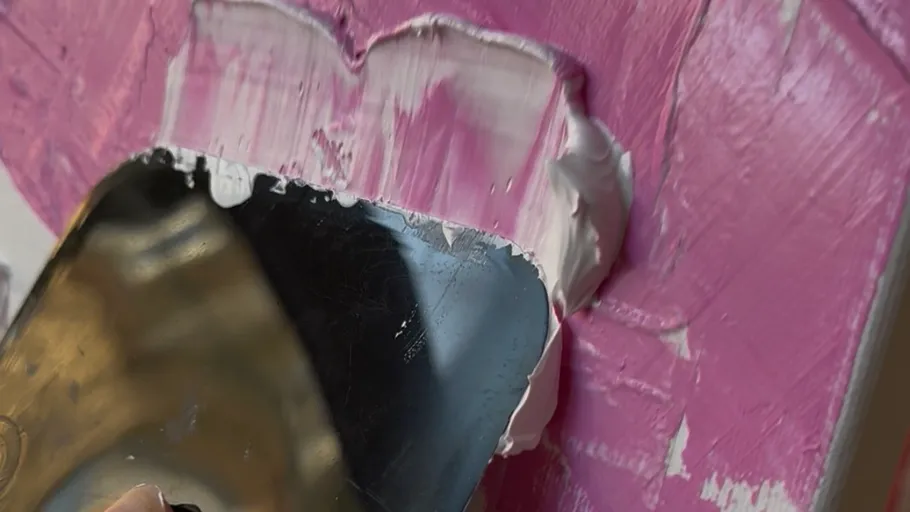 Painter spreads pink paint with a spatula.