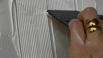 Hand verteilt weiße Paste mit Werkzeug.