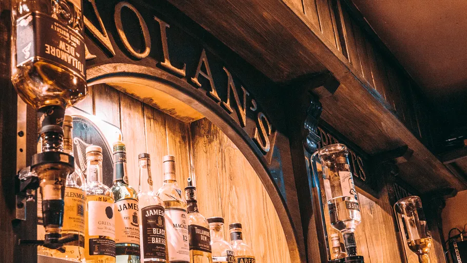 Multiple whiskey bottles displayed on wooden bar.