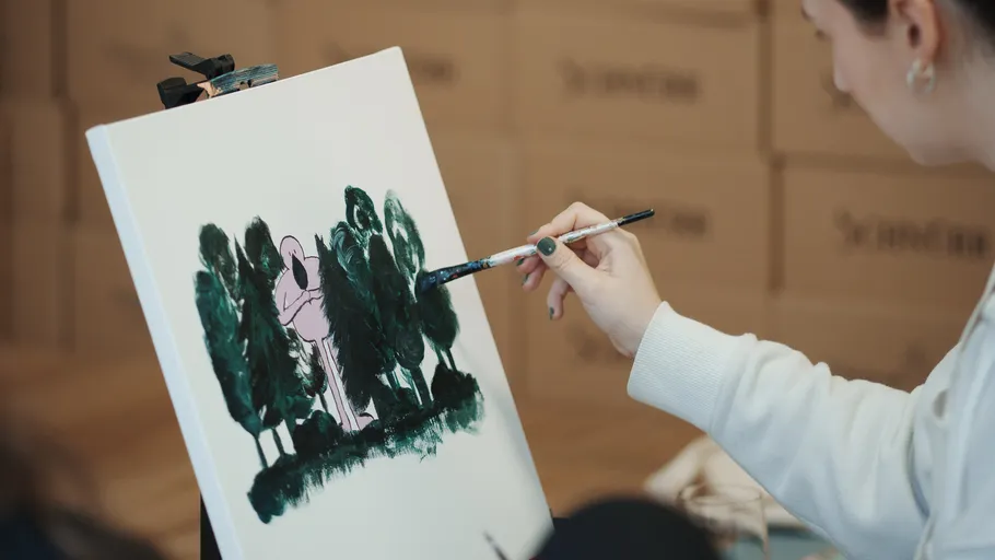 Person painting green trees on canvas indoors.