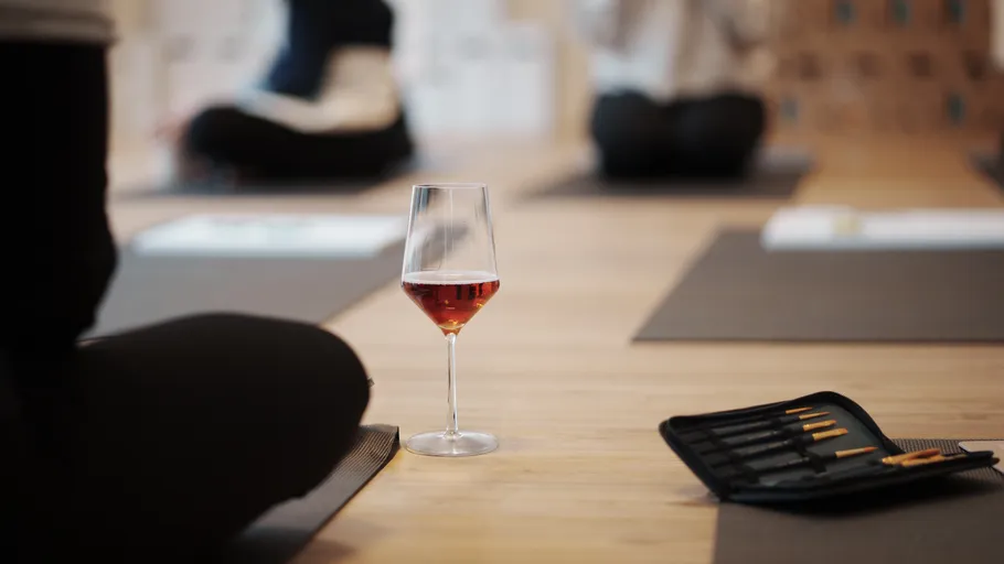 Wine glass on yoga mat, people meditating.