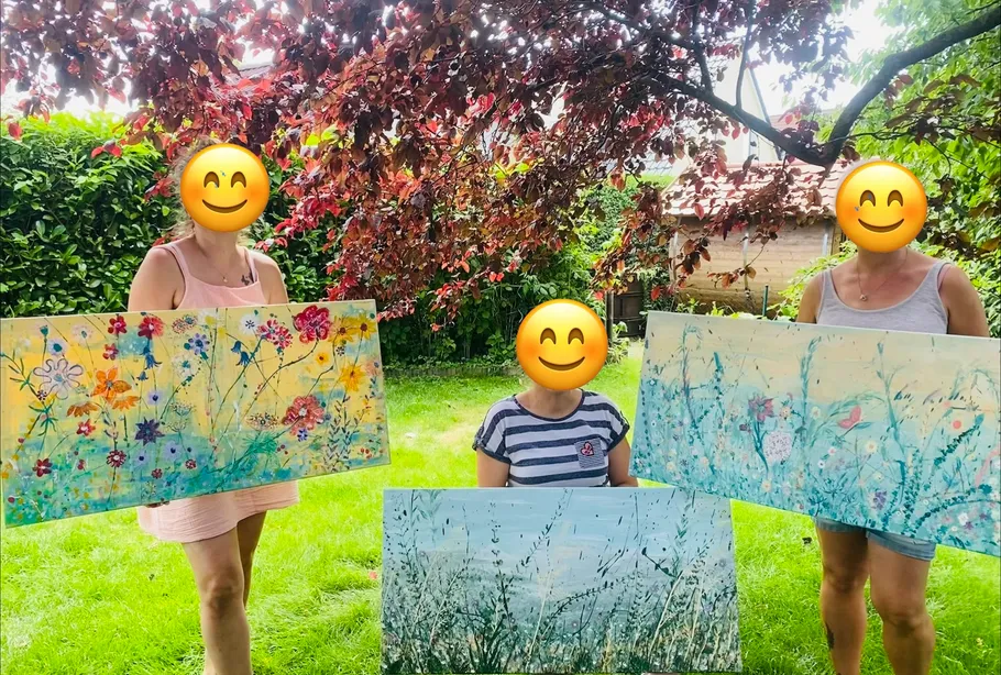 Three people holding paintings in a garden.