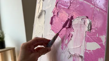 Hand trägt rosa Farbe auf Leinwand auf.