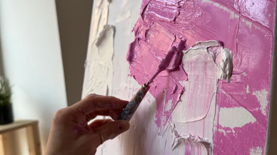 Hand applying pink paint on canvas.