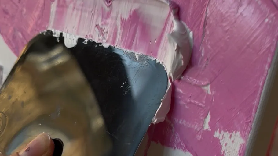 Palette knife spreads paint on canvas.