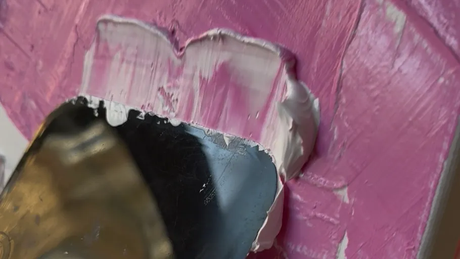 Malmesser verstreicht Farbe auf pinker Leinwand.