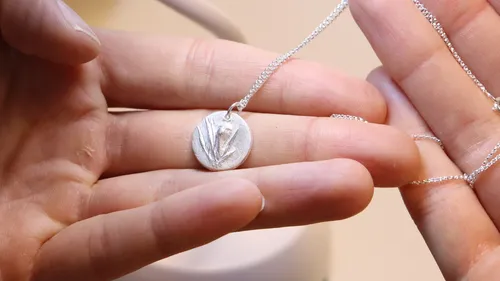 Hands holding a silver pendant necklace.