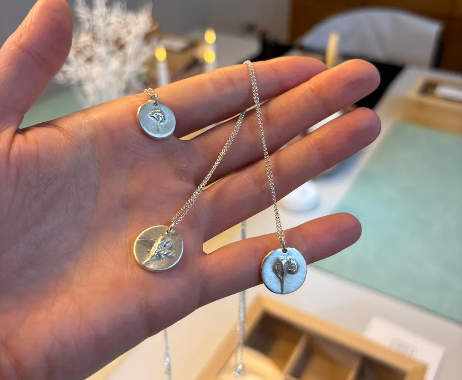 Hand holding necklaces with floral pendants indoors.