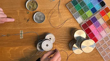 Person creating jewelry with beads on table.