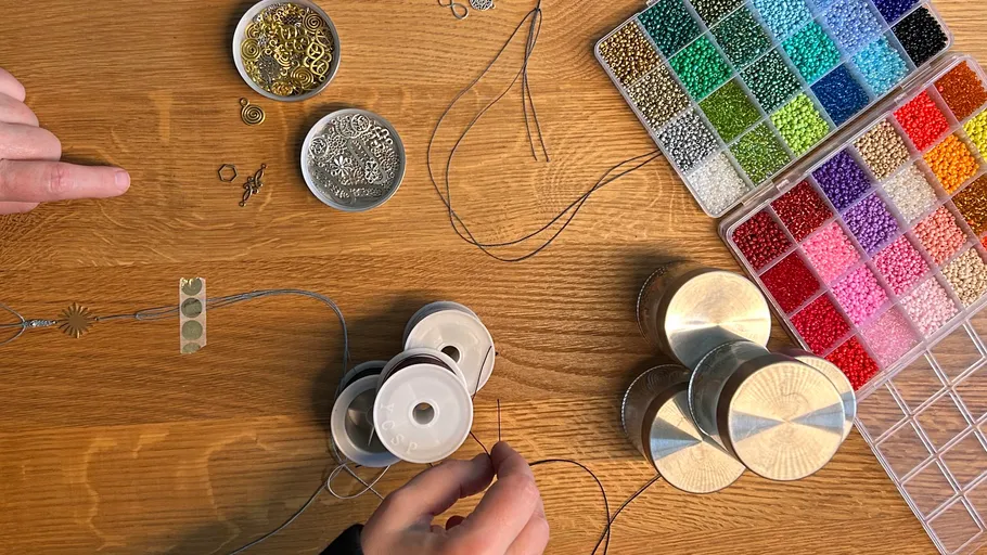 Person creating jewelry with beads on table.