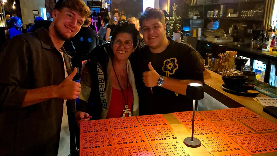 Drei lächelnde Personen in einer Bar mit Bingokarten.