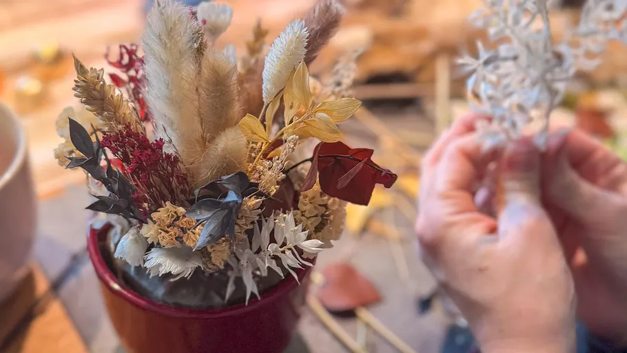 Hands arranging dried flowers in a vase.