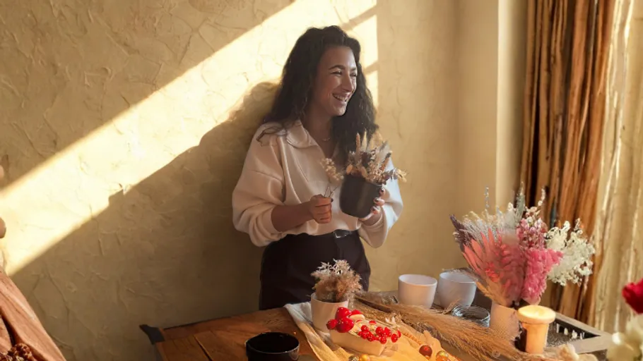 Woman smiling, arranging flowers on table.